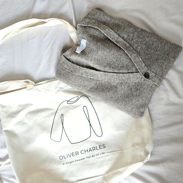A folded grey knit sweater resting on an Oliver Charles tote bag
