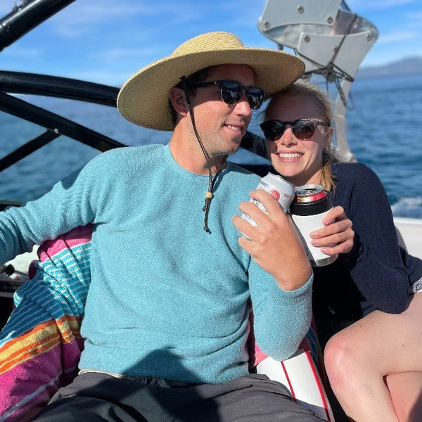 Two people outdoors in teal knitwear on a bright day by the water